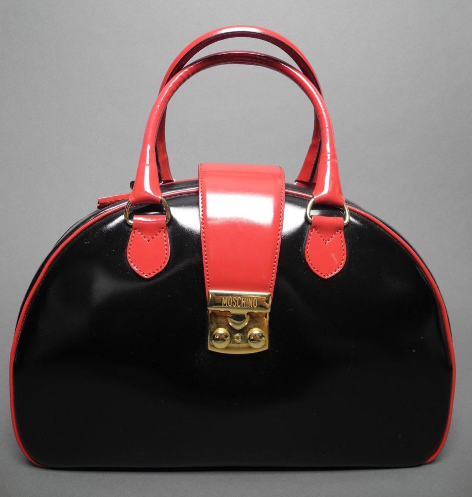 MOSCHINO

Sac en cuir vernis noir et rouge Rabas en cuir vernis rouge se terminant par un fermoir en métal doré Fermeture zippée rehaussée de pompons en cuir vernis rouge Double anses porté main L: 32 cm EN TRES BON ETAT