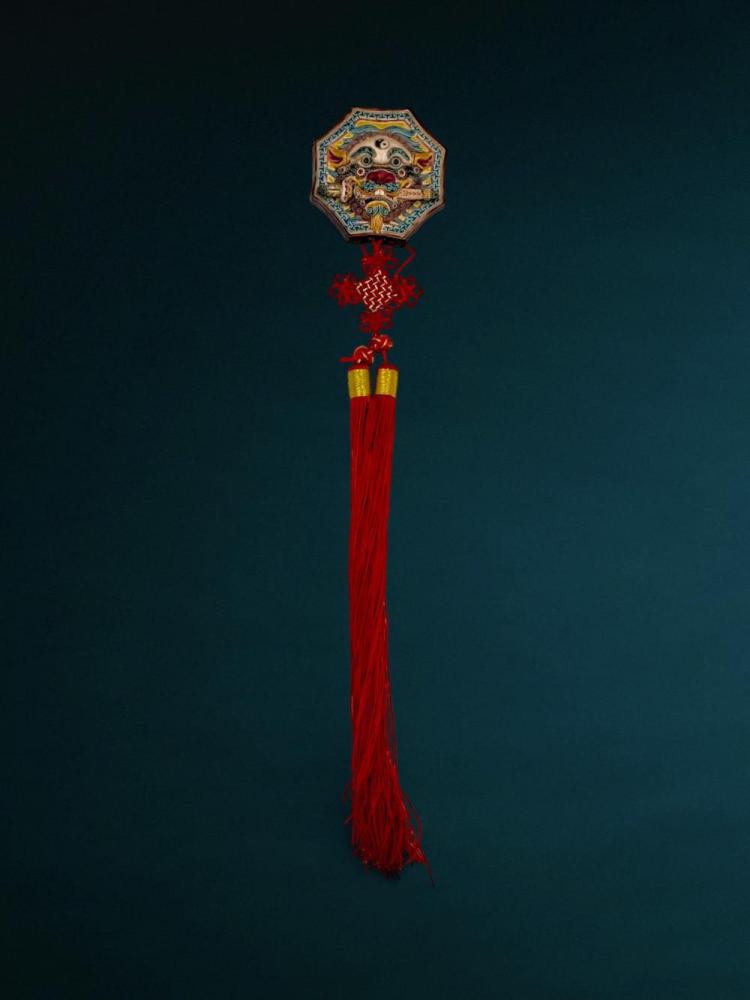 Description
Contemporary Chinese decorative wall hanging featuring an octagonal ceramic plaque with a sword-biting lion motif. The molded relief plaque is decorated in polychrome glazes with a Yin-Yang symbol and geometric fret border, integrated into a red textile assembly with a decorative Chinese knot and long double tassels. The reverse of the ceramic element is unglazed and lacks maker’s marks or inscriptions.
Dimensions: Not provided.