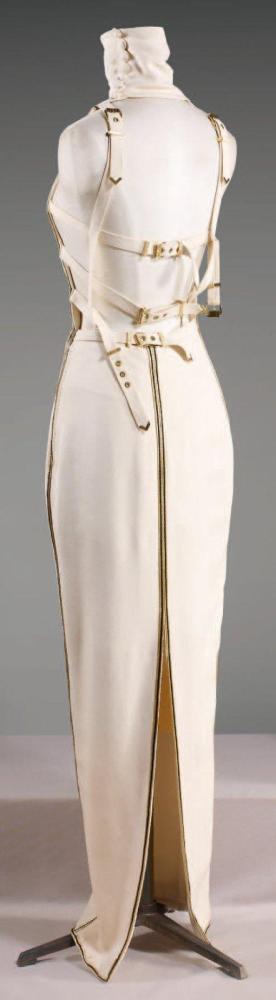 Gianni VERSACE

Robe longue en crêpe écru, col roulé boutoné sur la côté, profondes emmanchures américaines gansées de soutaches or, noire coutures de côtés à l’identique, dos nu jusqu’aux reinsorné de sangles ceintures à boucles en métal doré, jupe droite avec rappel des soutaches soulignant également la fente. (couture de la fente un peu décousue) Griffe noire, graphisme blanc, or