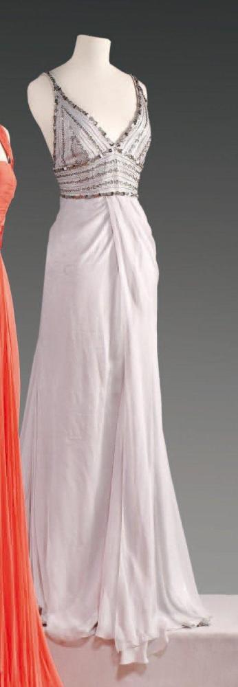 VERSACE par Donatella VERSACE, circa 2000

Robe du soir en mousseline grise perle, haut à poitrine dessinée sur bretelles brodées de perles, de strass, de rhodoid métallisé argent, effet de drapé sous la broderie par un panneau faisant portefeuille, jupe longue ample au dos par des quilles Griffe noire, graphisme beige