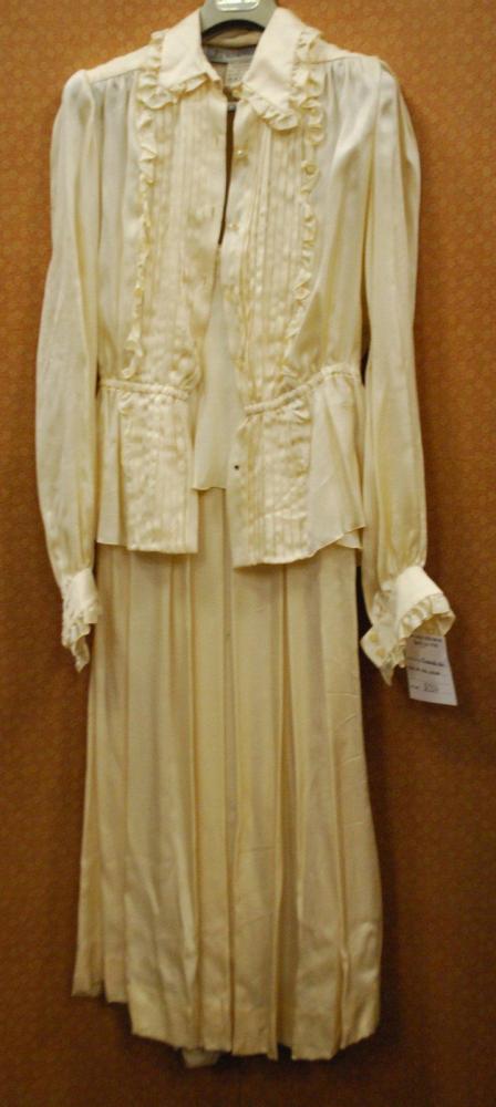 Jean-Louis SCHERRER Boutique circa 1978

Ensemble du soir en soie ivoire, haut de forme blouse à basque, à plastron plissé et volanté, petit col manches longues à poignets resserrés, jupe longue à plis recouverts à la taille d’un panneau au dos