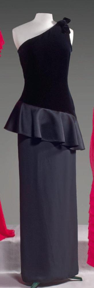VALENTINO

Robe longue, buste en velours noir à décolleté asymétrique sur une épaule ornée d’un noeud, volant de satin suivant la ligne du décolleté, jupe droite en crêpe de même couleur. Griffe blanche, graphisme marron