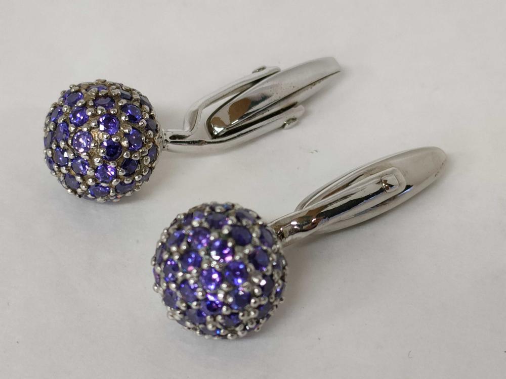 Description
Contemporary sterling silver and purple stone pave orb cufflinks. Each spherical head is densely pave-set with faceted purple stones and mounted on a fixed stem with articulated bullet-back toggles. The interior of the stems is incised with a 925 hallmark indicating sterling silver purity.
Orb Diameter: 10 mm
Total Length: 23 mm
Total Weight: 10.8 grams.