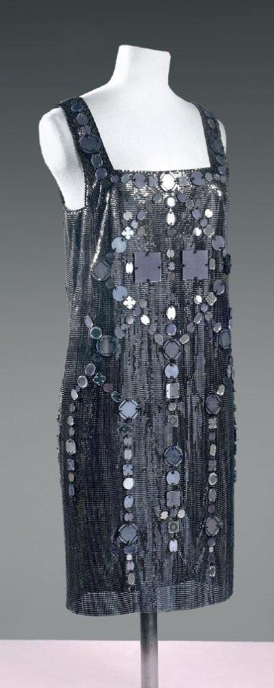 VERSACE par Donatella VERSACE, circa 2000

Robe de cocktail en cotte de maille noire ornée de miroirs de même couleur et de formes différentes formant des motifs géométriques, décolleté carré, larges bretelles, dos nu plongeant jusqu’aux reins. Griffe noire, graphisme beige