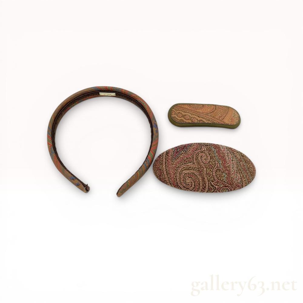 Description
Three Etro hair accessories featuring signature paisley patterns, late 20th century. The group includes one fabric-covered headband with braided cord trim, one small rectangular barrette with a suede-like backing, and one large oval barrette with a woven textile front. Each item bears an applied off-white plastic Etro brand tag, and both barrettes feature gold-toned metal spring-tension hardware.
Headband width: 13 cm
Small barrette length: 9 cm
Large barrette length: 11.5 cm.