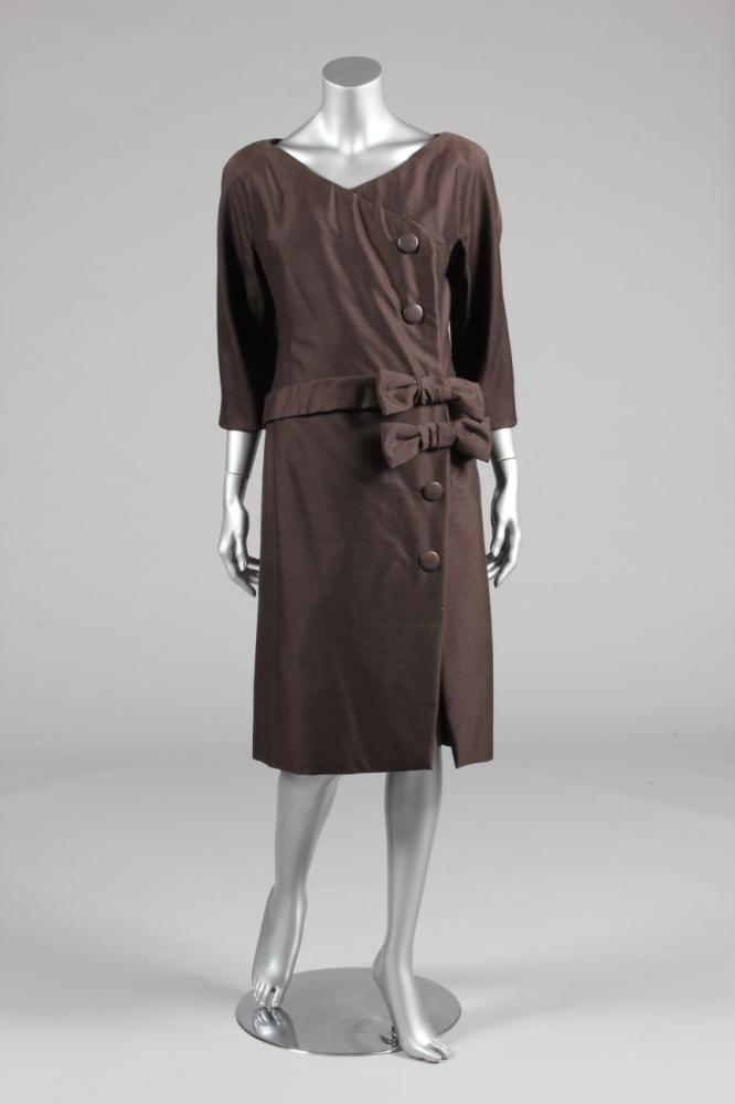 

A Christian Dior London brown wool dinner dress, early 1960s, labelled and numbered 10094 and size 14, with diagonal bodice fastening, the waist trimmed with two bows, bust 97cm, 38in
