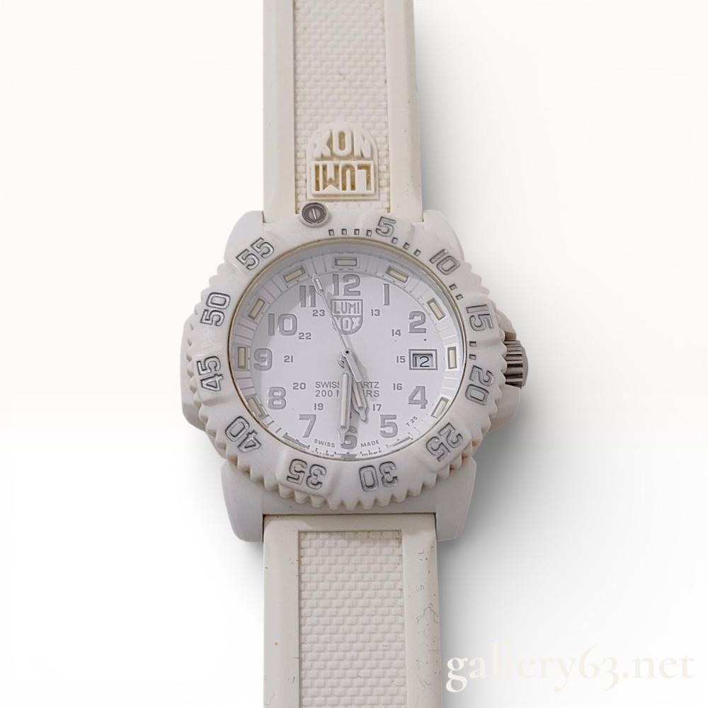 Description
Luminox Navy Seal Colormark 7050 Series Whiteout quartz wristwatch, reference 7057, purchased in 2019. The watch features a white polycarbonate reinforced fiberglass case, a unidirectional rotating bezel, and a white dial with tonal Arabic numerals, a date window at the 3 o’clock position, and tritium gas tube illumination. It is equipped with a Swiss quartz movement and is mounted on the original white silicone strap with a stainless steel tang buckle. The case back is embossed with the Navy SEAL eagle, trident, and anchor emblem and includes the original warranty card and user manual.
Case size: 38.2mm.