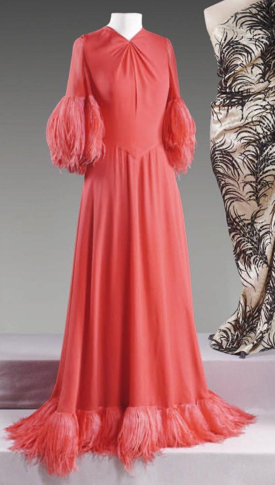 VALENTINO

Robe longue en crêpe rouge, encolure en v soulignée d’un drapé,demi manches , ourlet de la jupe ample gansés de plumes de cygnes lustrées à la couleur, effet de taille basse par une découpe en pointe. Griffe blanche, graphisme noir