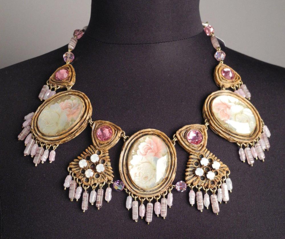 HENRY - circa 1960

Collier en résine gravée orné de cabochons rehaussés de pâte de verre à décor de roses se finissant par des pendeloques en pierres parmes Il est monté sur une chaîne en métal doré entrecoupée de pierres et perles en cristal roses Fermoir crochet Signé au revers d’un des éléments
