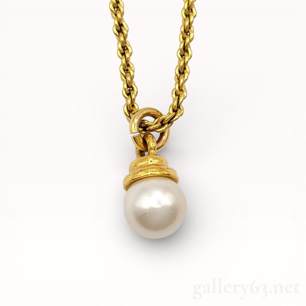 Description
Authentic Dior necklace featuring a gold-tone chain suspending a single round faux pearl pendant. Pearl mounted beneath a decorative gold-tone cap with textured detailing. Chain formed with uniform links and finished with an adjustable clasp. Design presenting a classic drop silhouette with restrained branding consistent with Dior costume jewelry.