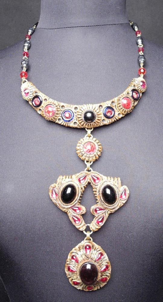 HENRY - circa 1960

Collier articulé en résine gravé ornée de cabochons en verre prune, rubis et noir monté sur une chaîne en métal doré entrecoupée de perles et d’éléments en rappel des teintes. Fermoir crochet Signé au revers d’un des éléments