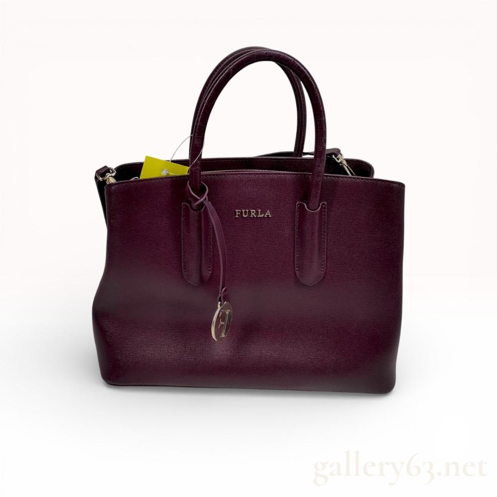 Description
Furla Tessa structured tote bag crafted from burgundy Saffiano leather with gold-tone hardware. The triple-compartment design features a central zippered section flanked by two compartments with magnetic snap closures, dual rolled top handles, and a detachable adjustable shoulder strap. Exterior details include metal brand lettering, a circular logo charm, and protective base feet, while the interior is lined in tonal logo-print fabric with one zippered and one slip pocket.
Width: 11.5 inches
Height: 9 inches
Depth: 5 inches.