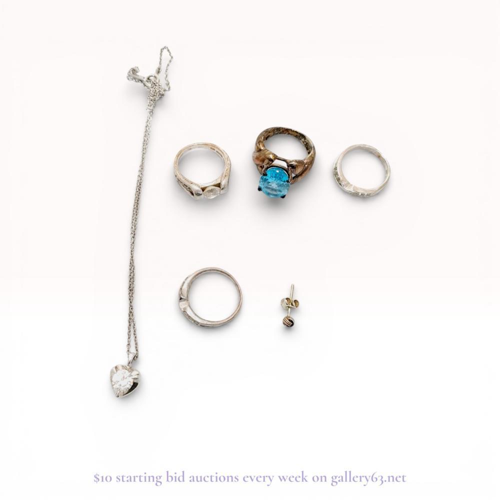 Description
An assortment of contemporary jewelry including a sterling silver heart pendant necklace, three silver-toned rings, and a single gold-toned ball stud earring. The necklace features a fine-link chain and a slider pendant set with a 1.45 carat heart-cut cubic zirconia. One ring is set with a large oval-cut blue stone in a leaf-motif setting, while the others feature clear accent stones. The pendant is marked SV925 and CZ 1.45 on the reverse.