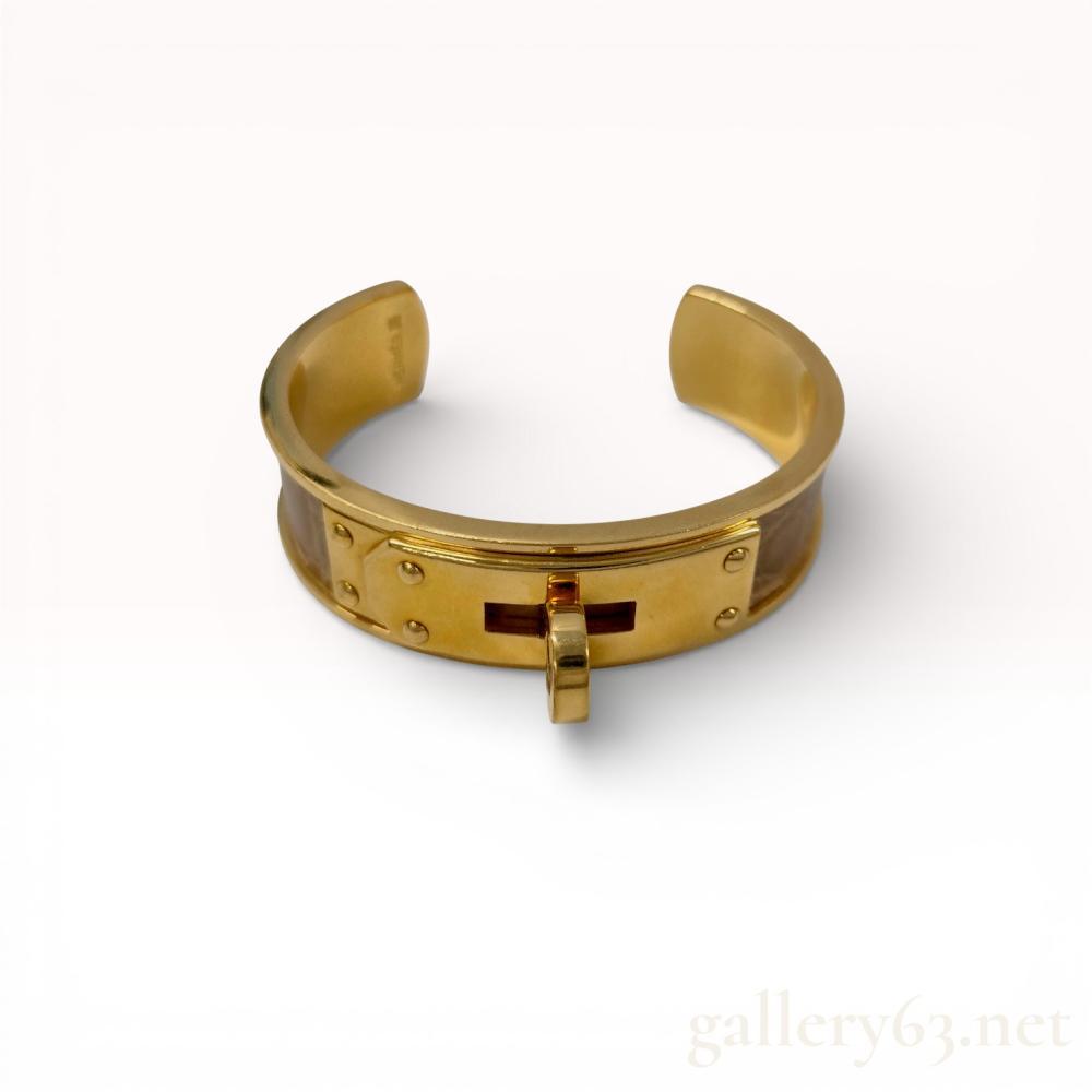 Description
Hermes Kelly Dog cuff bracelet featuring gold-toned metal and a light taupe exotic skin inlay. The design includes the signature turn-lock hardware and studded plates on an open-back cuff frame. The interior is incised with the HERMES mark and a square hallmark containing a symbol and the letters CPL.
Interior circumference: 15 cm.