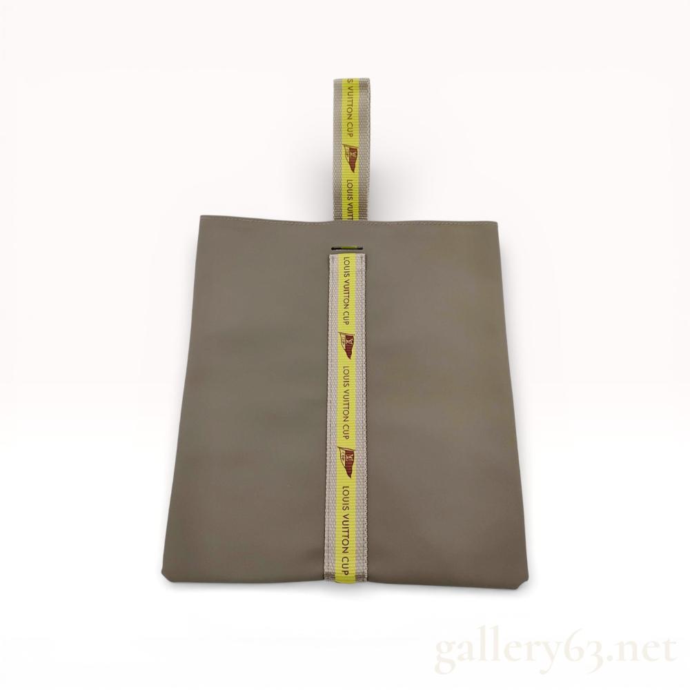 Description
Louis Vuitton accessory pouch from the Louis Vuitton Cup collection. The item is constructed from a taupe matte coated exterior with a water-resistant white coated interior and a vertical woven nylon strap. The tan and yellow webbing features repeated brown text reading LOUIS VUITTON CUP alongside a pennant logo. No date codes or serial numbers are visible.
Width: Approximately 23 cm (9 inches).
