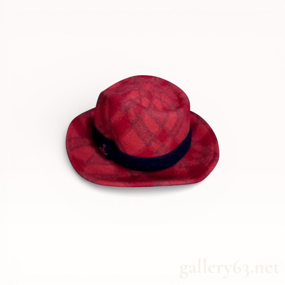 Description
Vivienne Westwood fedora hat, late 20th to early 21st century. The hat is constructed from 100 percent brushed wool in a red and charcoal grey plaid pattern with a navy blue felt band and a red metal orb logo pin. The interior features an unlined crown, a black grosgrain ribbon sweatband, a woven designer label, and a Japanese care tag.