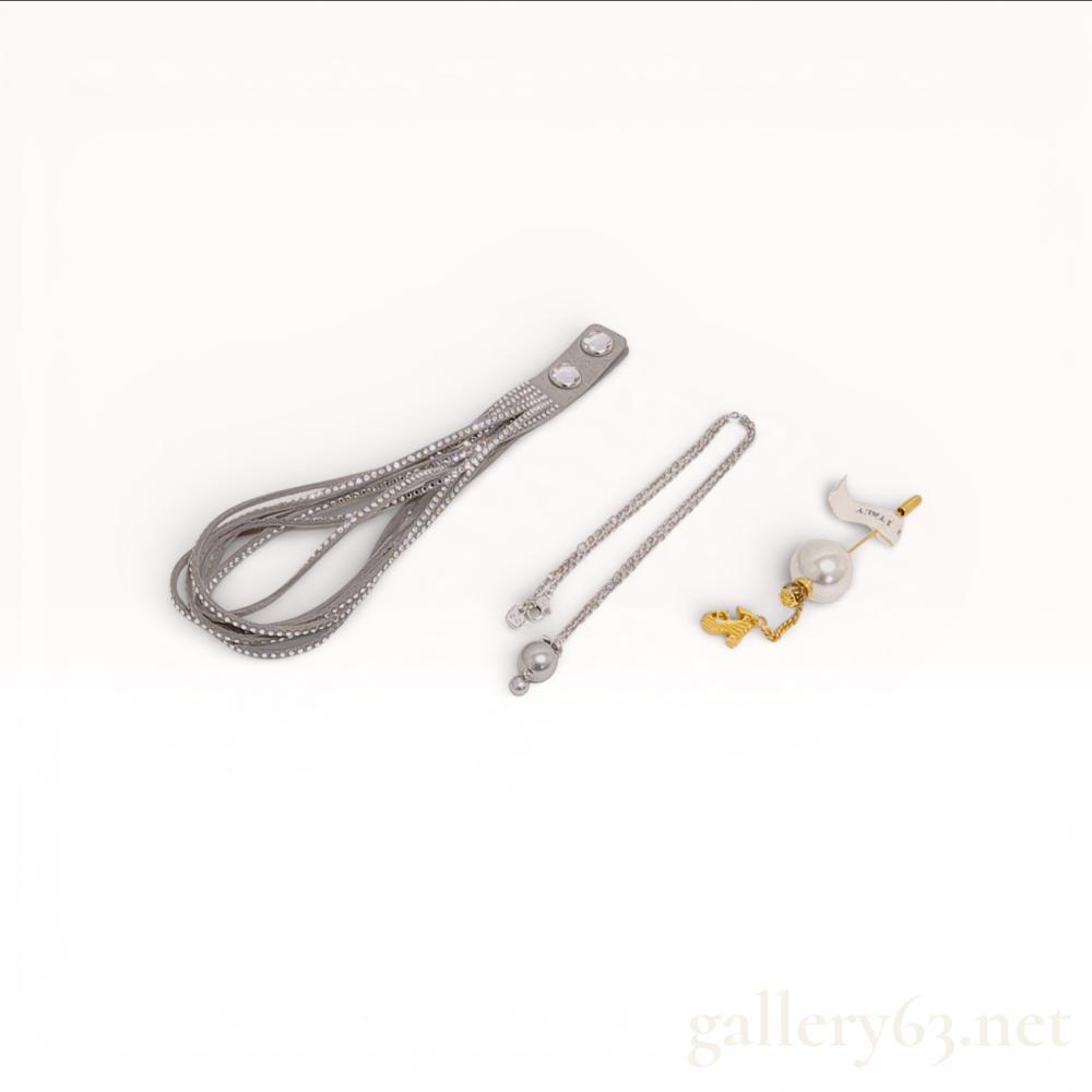 Description
This lot consists of three contemporary designer accessories from Swarovski and Salvatore Ferragamo. The first item is a Swarovski Slake grey Alcantara wrap bracelet, model 5181989, featuring multiple strands of synthetic suede embellished with rows of clear faceted crystals and finished with silver-tone snap closures. The second item is a Swarovski pendant necklace in silver-tone rhodium plating, featuring two graduated grey simulated pearls and signed with the Swarovski swan logo on the extension chain hangtag. The third item is a Salvatore Ferragamo stick pin in gold-tone metal, featuring a large white simulated pearl and a dangling wedge shoe charm signed Ferragamo. The collection is accompanied by original presentation packaging including two blue Swarovski boxes, one Swarovski velvet pouch, one red Salvatore Ferragamo box, and a Ferragamo branded polishing cloth.