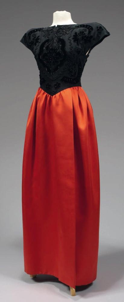 VALENTINO

Robe du soir longue, haut en ottoman noir rebrodé d’applications de velours ornées de perles de jais de soutaches rehaussées de marcassites, encolure bateau, épaules raglan tombantes, jupe à effet de portefeuille en satin rougeà taille basse par un découpe et légèrement froncée. Griffe blanche, graphisme marron