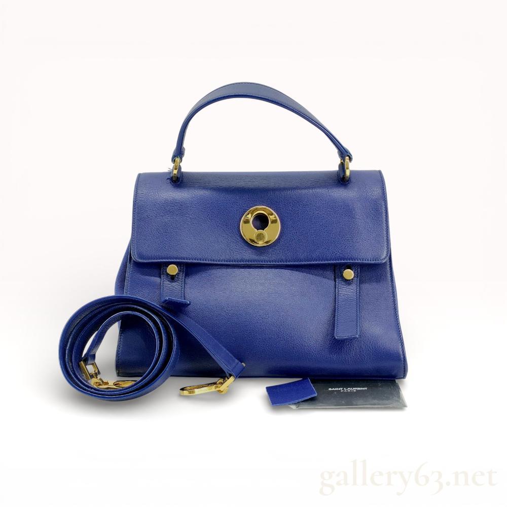 Description
Saint Laurent Paris Muse Two top handle bag in cobalt blue grained leather with tonal canvas lining. The exterior features a front flap with a gold-tone keyhole lock, decorative vertical straps, a rear slip pocket, and a protective footed base. The interior is divided into two compartments by a central zippered partition and includes a detachable leather shoulder strap and brand card.
Approximately 12 inches W x 8.5 inches H x 6 inches D.