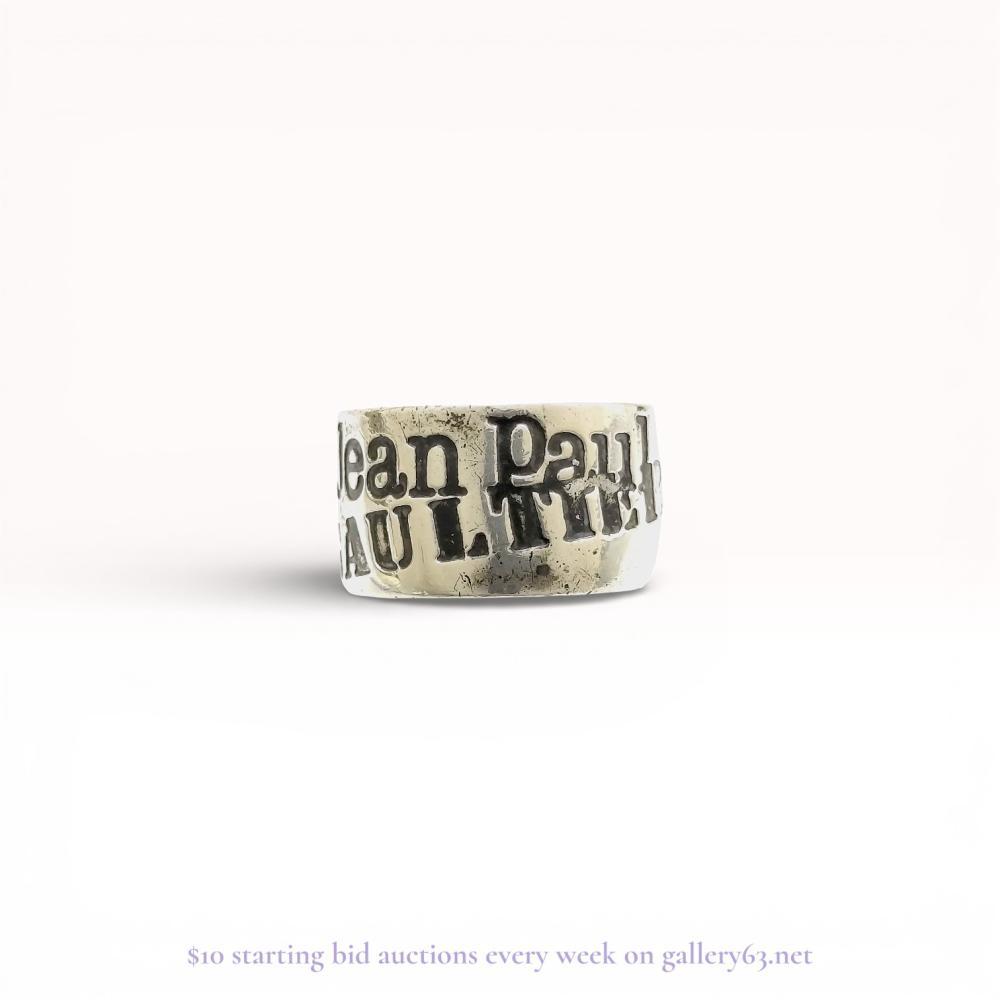 Description
Jean Paul Gaultier sterling silver logo band ring. The wide, flat-profile band features the designer name in bold relief block lettering across two offset rows. The interior of the band is incised with the mark SILVER 925.
Internal diameter: 20mm (US size 10.25)
Band width: 12mm.