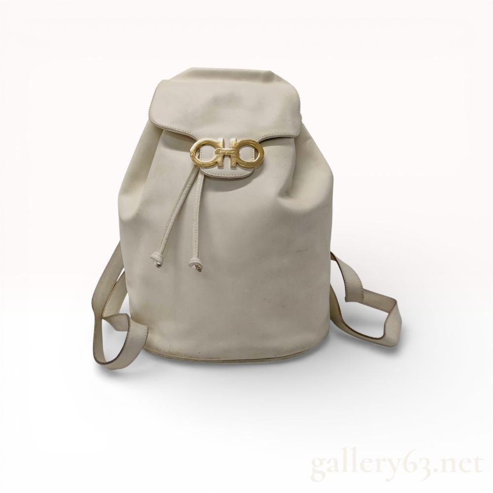 Description
Salvatore Ferragamo Gancini drawstring backpack featuring off-white leather construction and gold-tone hardware. The exterior includes a front flap with a signature Gancini flip-lock closure, a drawstring top, and adjustable leather shoulder straps. The interior is lined in black jacquard fabric with a single zippered pocket and an interior leather tag stamped Salvatore Ferragamo, BV-21 6148, and Made in Italy.