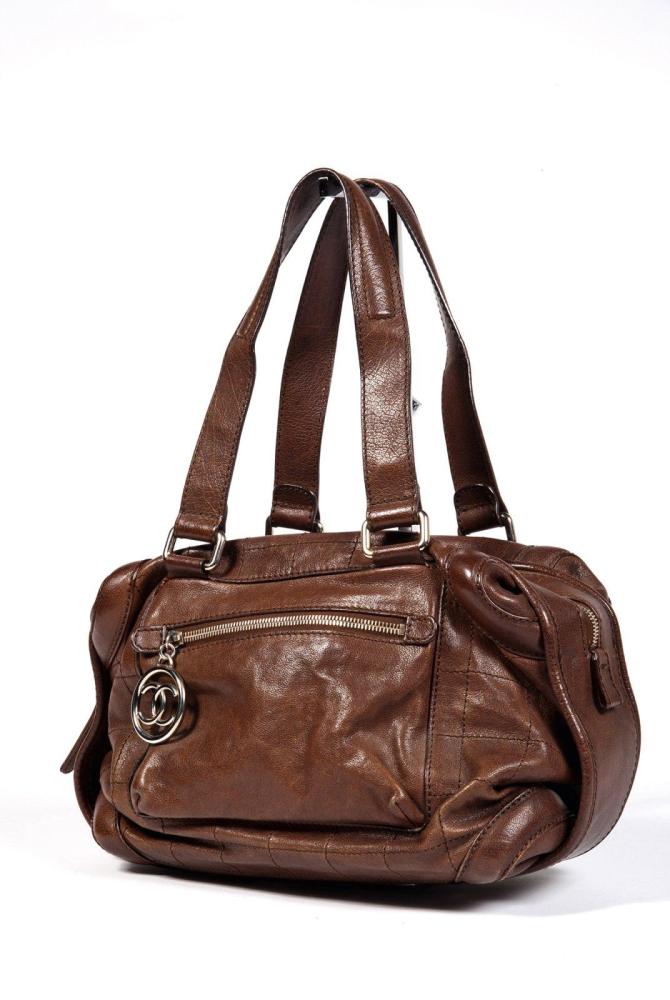 CHANEL

Sac 34 cm en cuir marron à surpiqûres ton sur ton a effet matelassé, fermeture éclair, double demi-anses bandoulières, poches extérieures zippées dont un curseur retenant le sigle de la Maison en acier chromé.Bon état. (légères égrenures)