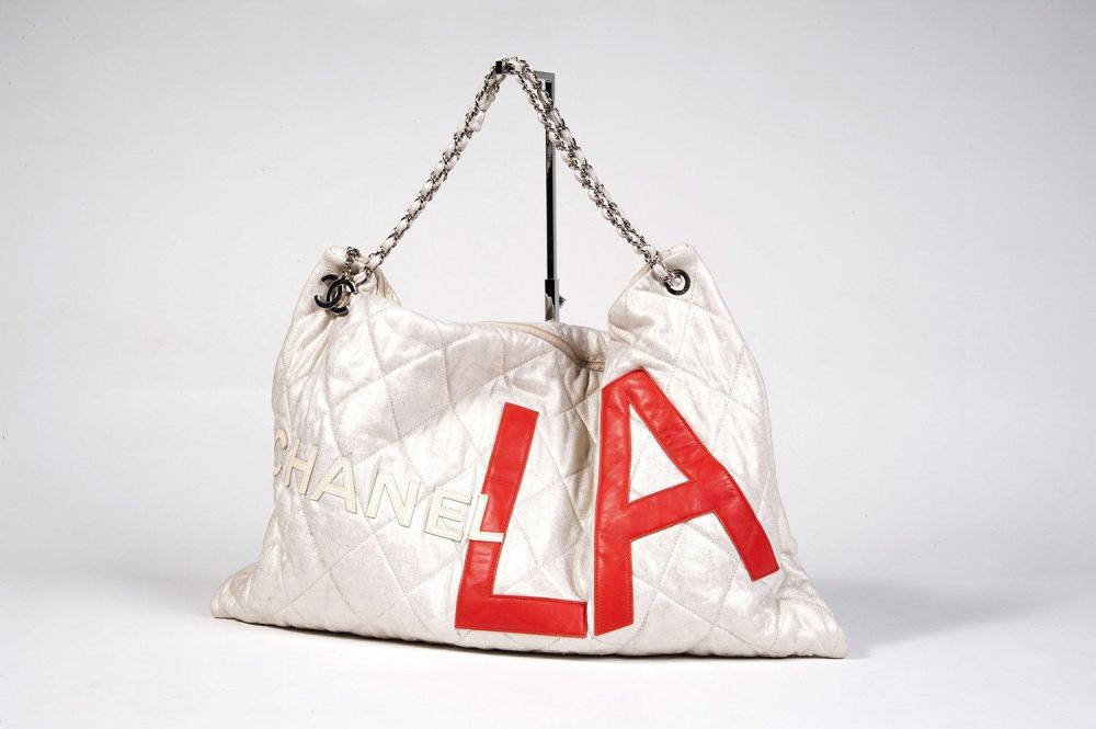 CHANEL

Sac XXL 56cm en coton matelassé métallisé or, devant rehaussé de lettres en cuir agneau figurant "CHANEL LA", fermeture éclair, anse chaîne réglable en acier chromé entrelacée de coton en coordonné, se terminant par un sigle à l’indentique. Bon état