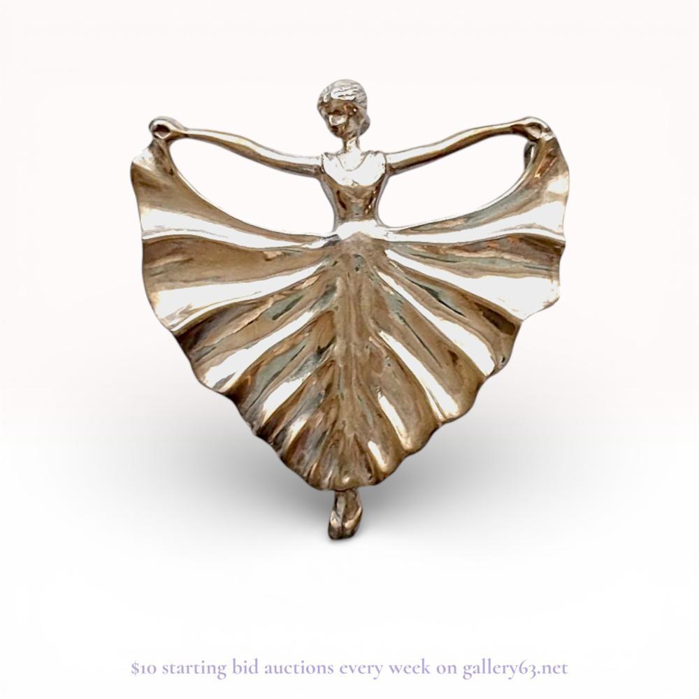 Description
Japanese figural ballerina brooch, mid-20th century. High-grade silver construction featuring a dancer with outstretched arms holding a pleated skirt in a design resembling the Sonia pattern by Marcel Boucher. The reverse is stamped with an oval cartouche containing the Japanese characters for pure silver and the word SILVER.
42mm x 35mm.