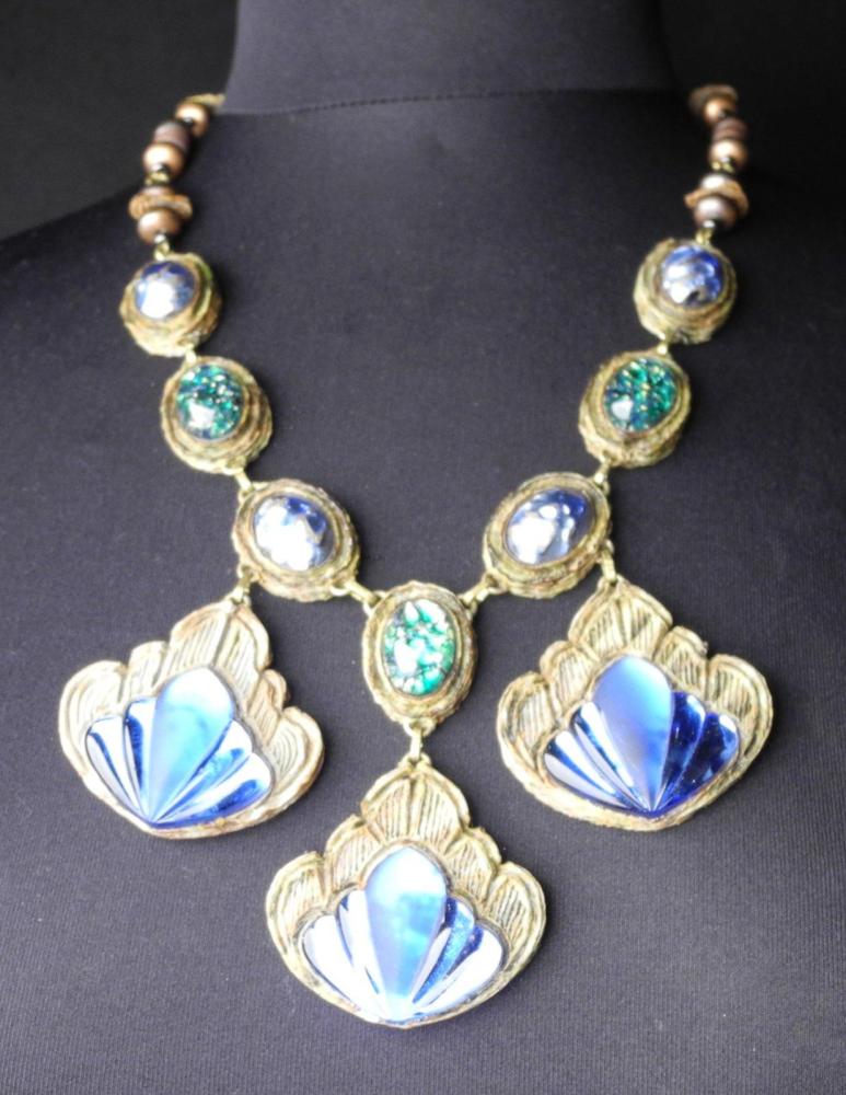 HENRY - circa 1960

Collier en résine gravée ornée de 3 pendants rehaussés de pâte de verre bleue et verte monté sur une chaîne en métal doré entrecoupée de perles Fermoir crochet Signé au revers d’un des éléments