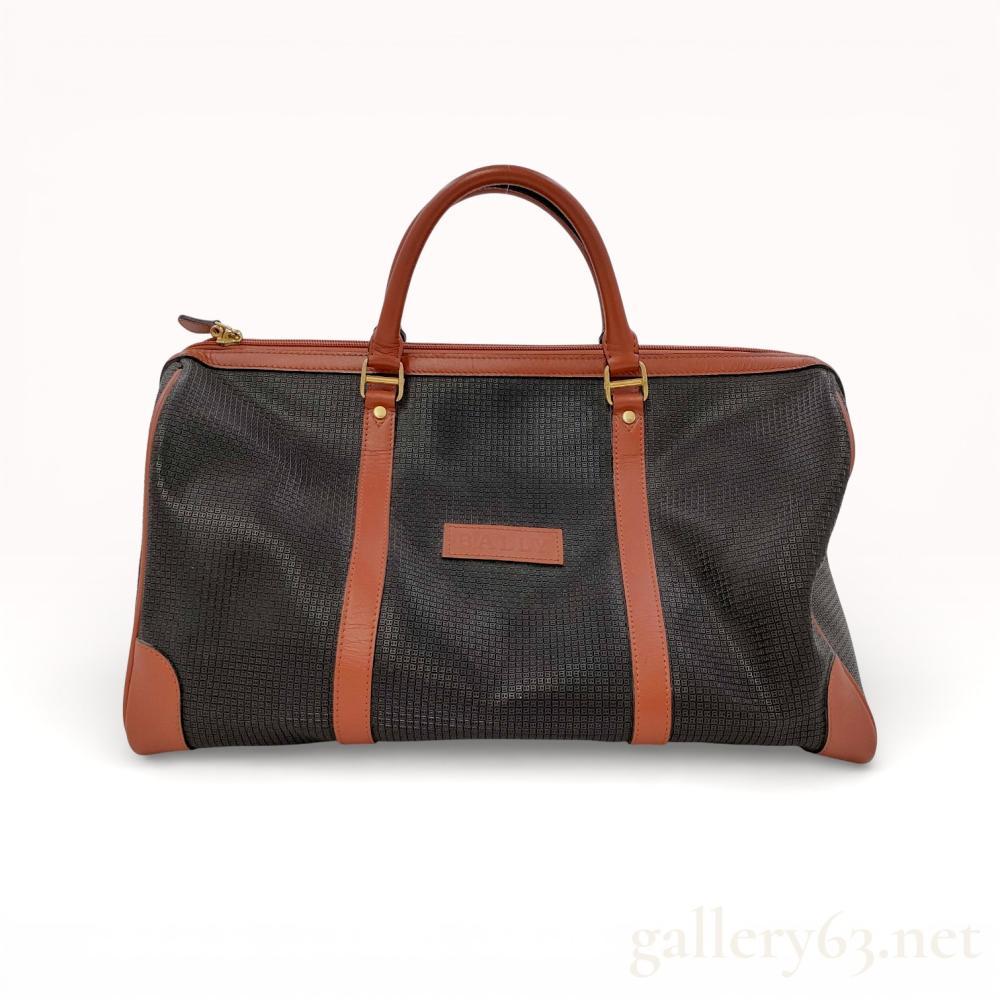 Description
Bally weekender duffle bag, late 20th century. The bag features a dark gray coated canvas body with an all-over embossed repeating B logo pattern accented by cognac-colored smooth leather trim. It is designed with rolled top handles, vertical support straps, reinforced corners, and a tan leather-lined interior containing a zippered side pocket. A leather Bally patch is affixed to the front exterior, and a gold-tone metal brand plaque is located on the interior.
Approximately 18 to 20 inches in length.