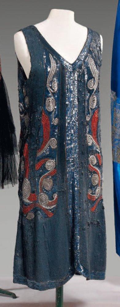 Anonyme

Robe pailleté gris foncé, gris argent à effet de rayuressoulignées de petites perles de verre viel or, rehaussé également de motifs Art Nouveau multicolore décolleté en pointed’un biais de paillettes,bas de la robe à l’identique avec un lége arrondi sur le devant, sans manches