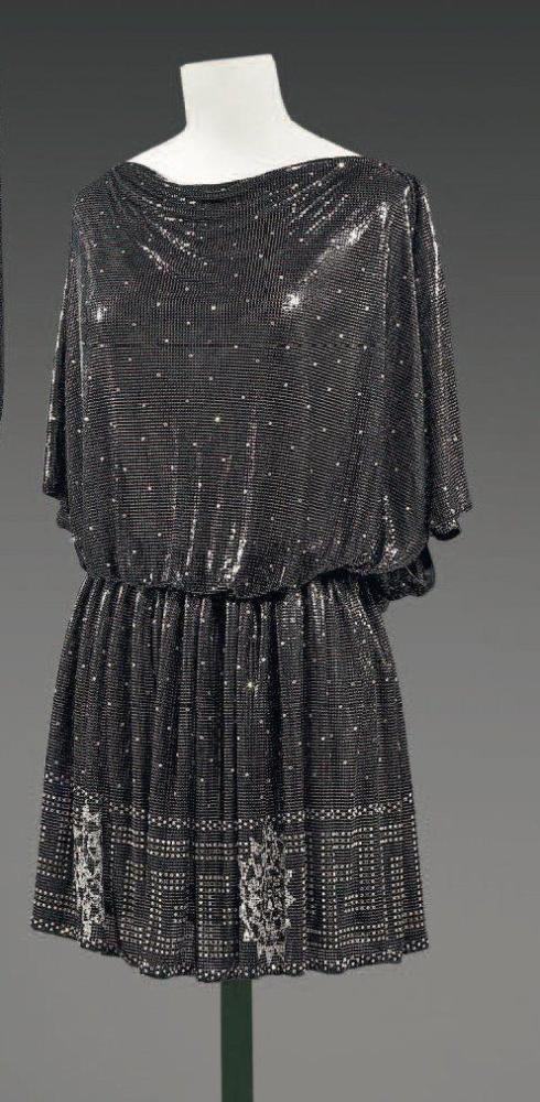 Gianni VERSACE

Robe de cocktail de forme" tunique antique" en cotte de maille noire parsemé de strass, décolleté bateau bénitier , manches courtes raglan, bas de la jupe à motif d’une grecque et de soleils stylisés Griffe noire, graphisme blanc, or