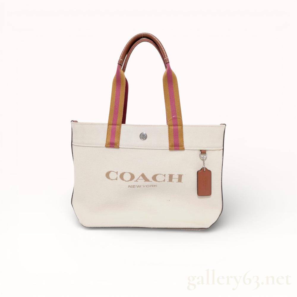 Description
Coach Canvas Tote 20, model CK168, contemporary. The bag is constructed from off-white canvas with a smooth brown leather base and trim, featuring striped webbing handles in mustard and burgundy with leather grips and contrast stitching. The front displays a printed Coach New York logo and a silver-tone snap button, while the interior contains a textile lining and a leather creed patch.
Approximately 11 inches W x 8 inches H x 5 inches D.