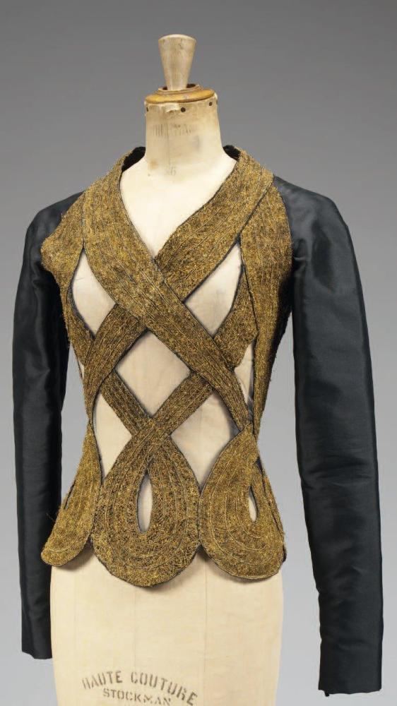 Atelier VERSACE, circa 1987 / 1990

Magnifique haut en tulle gris orné en applications de passementerie or soulignant un encolure en v, formant des croisillons pour terminer en boucles, dos et manches longues raglan en soie noire. (petits fils tirés) Griffe blanche, graphisme noir