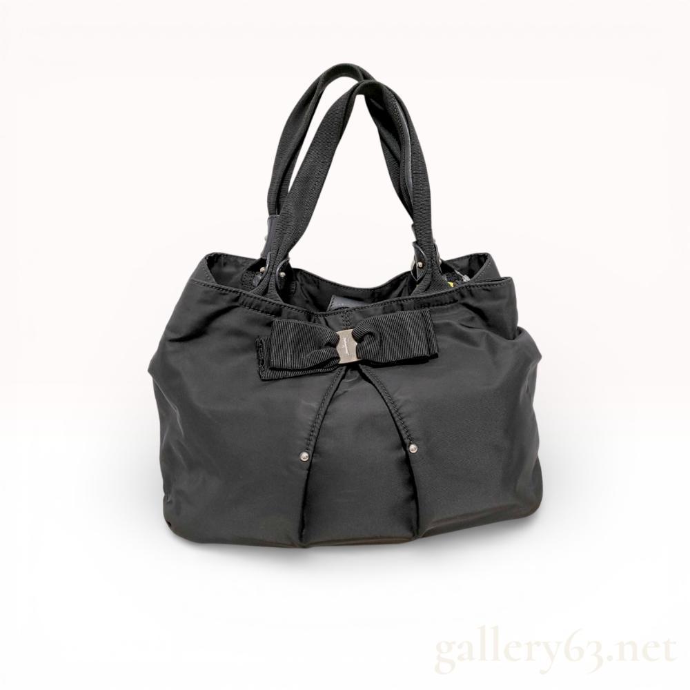 Description
Handbag in black nylon with soft gathered top and rounded body. Double top handles in black leather. Front Vara bow motif with small silver-tone Ferragamo plate at center. Drawstring tie detail at front with metal tips. Open top with interior zip pocket and fabric lining. Includes Ferragamo dust bag and cards shown. Light wrinkling and minor surface wear consistent with use.
