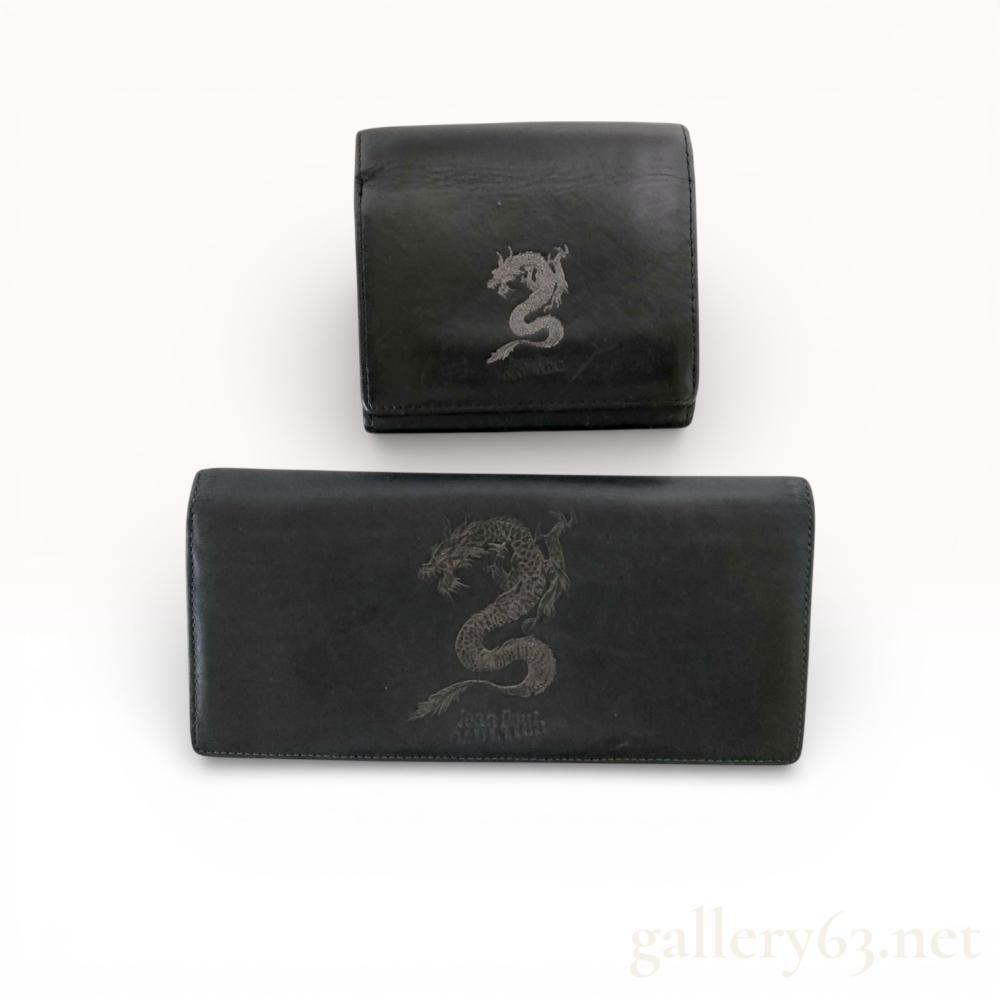 Description
Jean Paul Gaultier set of two wallets featuring an embossed dragon motif, late 20th to early 21st century. The lot includes one continental long wallet with a silver-tone interior zipper and one compact wallet with a silver-tone kiss-lock clasp. Both pieces are constructed from smooth black leather and bear the embossed Jean Paul Gaultier signature on the exterior and interior.
Length: 19 cm (long wallet).