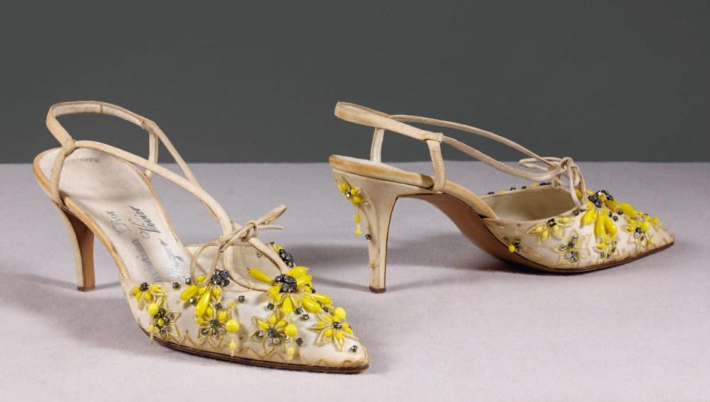 Christian DIOR par Roger VIVIER, circa 1955 / 1958

Paire de salomés en soie coquille d’oeuf brodé de perles de verre jaune à motif floral rehaussé de strass façon brillant, empeigne ressérée par un lien de cuir , lanières à l’dentique, talon "étrave" bout en" tête d’oiseau". (manque) Griffe au tampon argent sur la première semelle de propreté avec inscription "sur mesure"