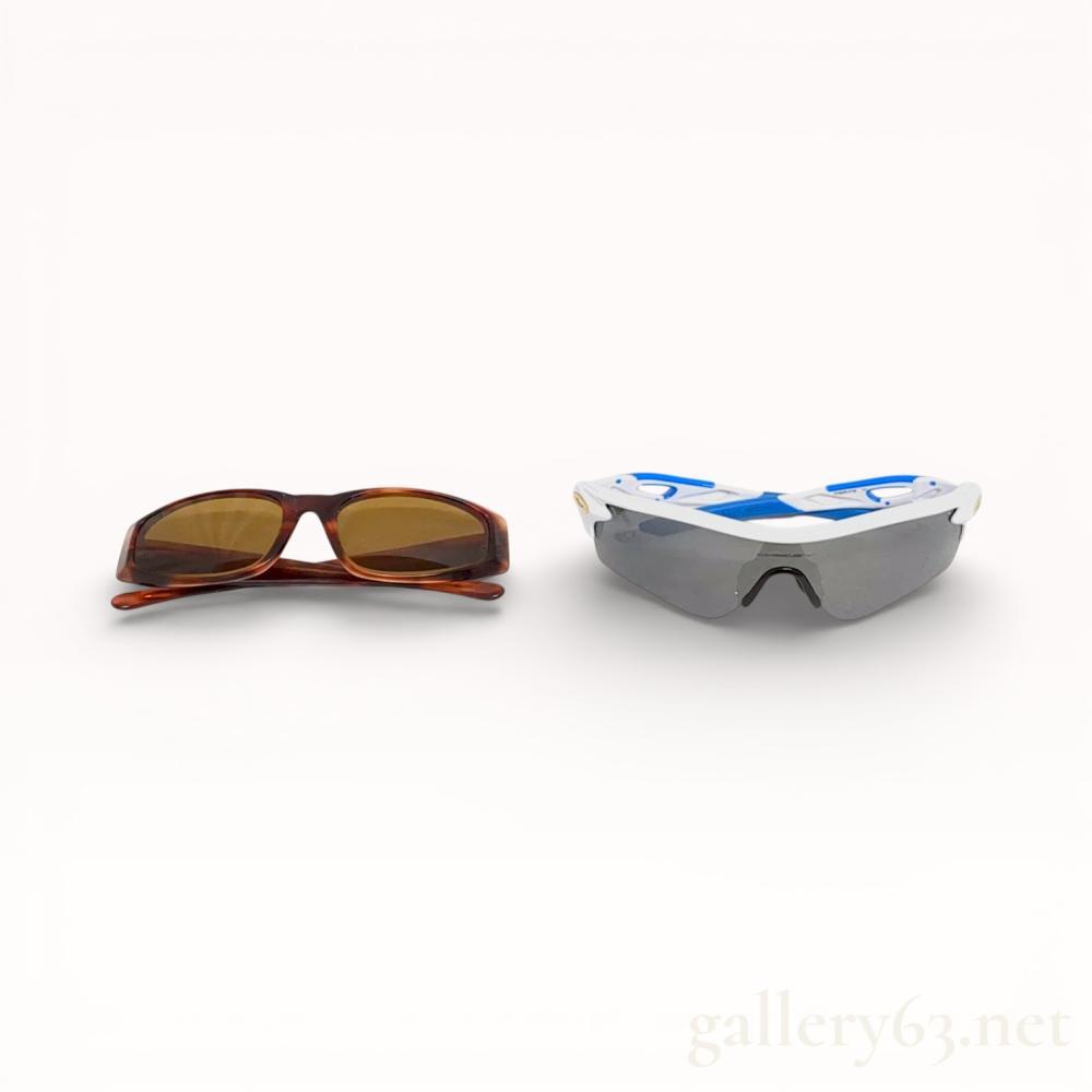 Description
A pair of Ray-Ban tortoiseshell acetate sunglasses and a pair of Oakley performance sport sunglasses. The Ray-Ban frames feature brown tinted lenses and a gold-tone swan emblem on the left temple, while the Oakley pair features a two-tone white and blue composite frame with a single-piece smoke grey lens. Accessories include a Ray-Ban pebbled-texture case and cloth, and an Oakley hardshell case, drawstring bag, and additional nose piece.
Oakley width: approximately 16 cm.