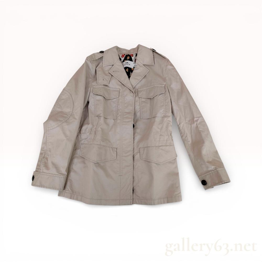 Description
Coach New York utility-style field jacket in a light beige cotton with a multi-colored floral polyester lining. The garment features four front patch pockets with button-flap closures, shoulder epaulets, reinforced elbow patches, and an interior adjustable drawstring waist. Construction includes a full-length metal zipper with a button-front placket and adjustable button cuffs.
Length: 27.5 inches.