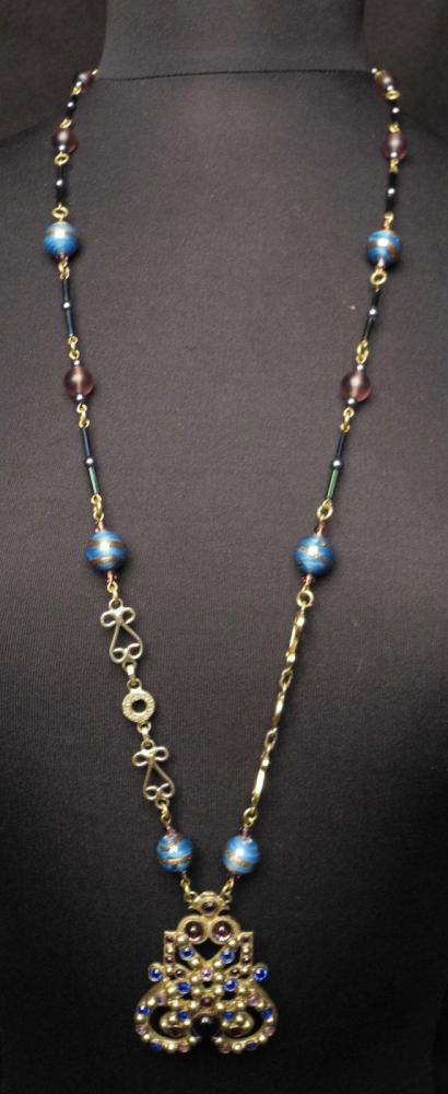 HENRY - circa 1960

Sautoir orné d’un pendentif rehaussé de cabochons en pâte de verre bleue et parme monté sur une chaîne en métal doré entrecoupée de perles en pâte de verre bleue à filets dorés et parme Fermoire crochet Signé au revers du pendentif