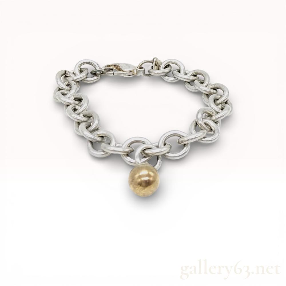 Description
Tiffany and Co sterling silver link bracelet featuring a single spherical charm. The piece is constructed of interlocking round silver links and a gold-tone ball charm secured with a lobster claw clasp. A circular hang tag is stamped 925 on one side and TIFFANY and CO on the reverse.
Length: Approximately 7.5 to 8 inches.