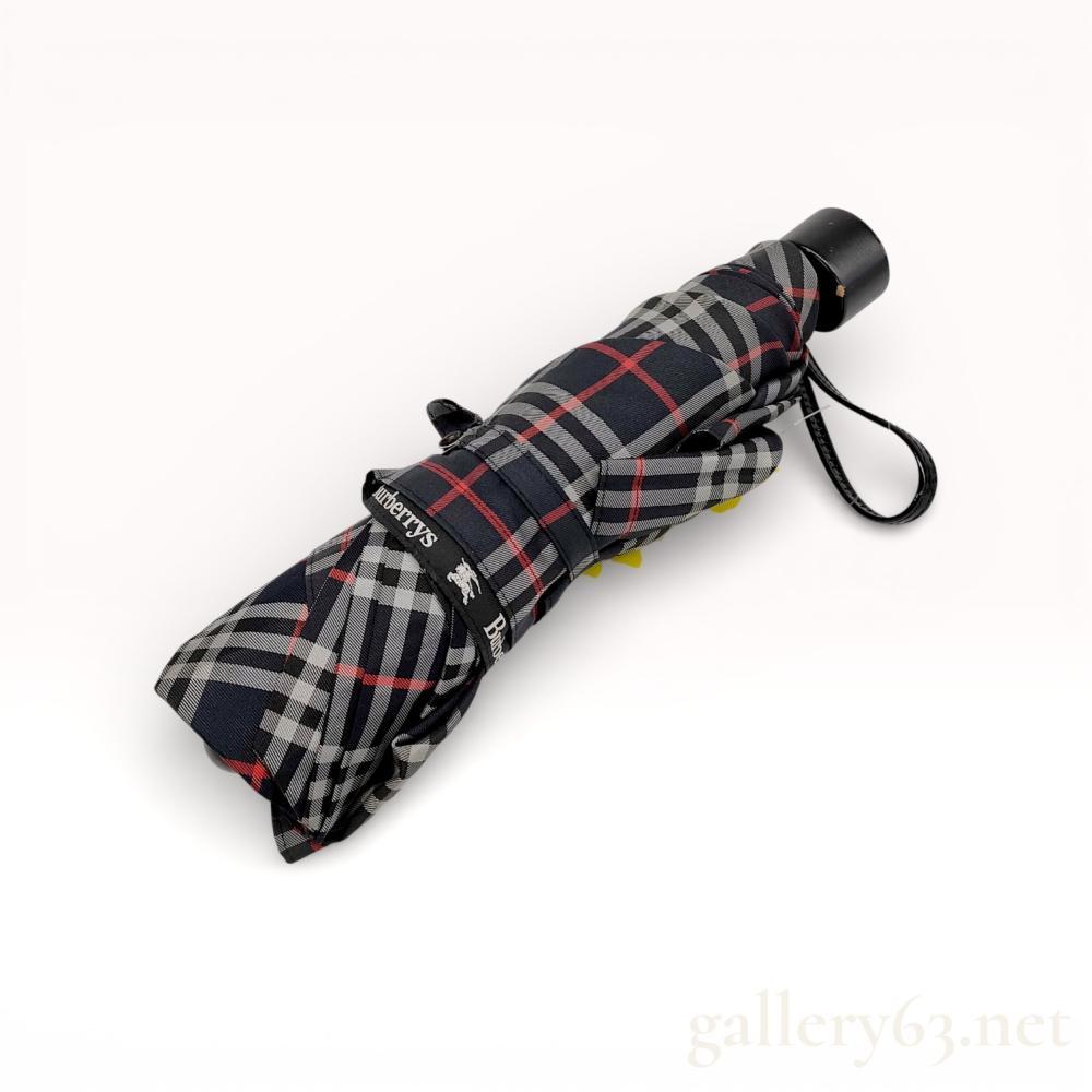 Description
Burberrys telescopic folding umbrella featuring a navy blue, white, and red check pattern, late 20th century. The piece is constructed with a synthetic fabric canopy, black-finished metal shaft and ribs, and a molded plastic handle with an integrated wrist strap. It includes a matching fabric storage sleeve and bears the Burberrys name and Prorsum knight logo on the canopy border, closure strap, and handle base.
Folded Length: 9.5 inches
Extended Length: 22 inches
Canopy Diameter: 38 inches.