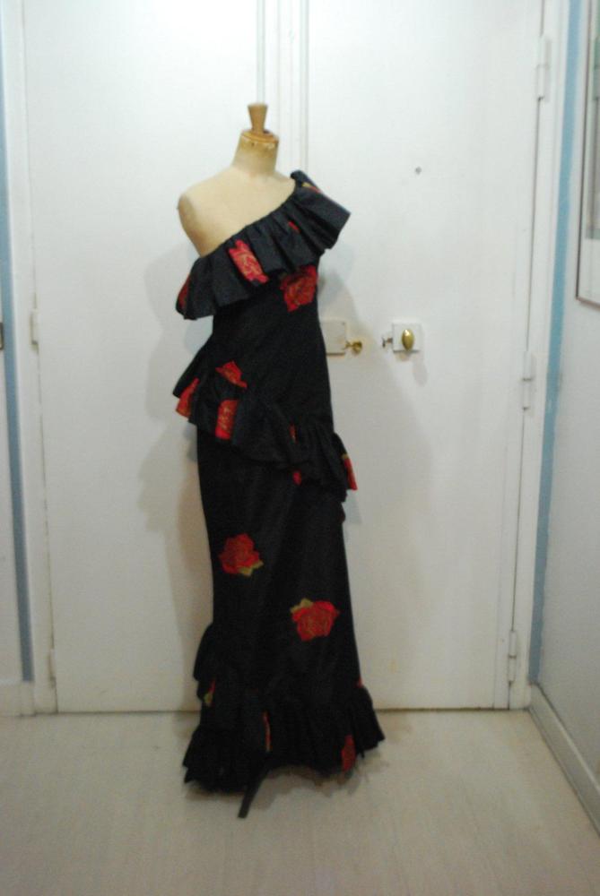 CAPECCI Genova, circa 1985

Robe longue en soie façonnée de petits pois sur fond noir ton sur ton rehaussé d’un imprimé floral rouge, vert, décolleté asymétrique souligné d’un volant, hanches et ourlet de la jupe droite à l’identique Griffe blanche, graphisme noir