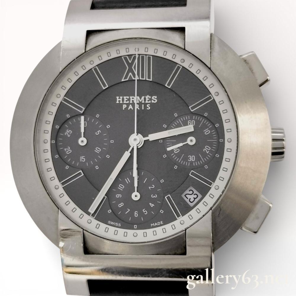 Description
Hermès Nomad autoquartz chronograph wristwatch featuring a brushed stainless steel round case with integrated lugs and crown guards. Dark gray dial signed Hermès Paris, set with applied Arabic and Roman numeral hour markers, baton hands, and three recessed chronograph subdials. Date aperture positioned near the 4 oâclock marker. Fixed stainless steel bezel with minute track. Case fitted with chronograph pushers and a signed crown. Exhibition-style case back engraved with Hermès branding and model details. Watch fitted with a black strap secured by a stainless steel deployant clasp. Serial 1894118
