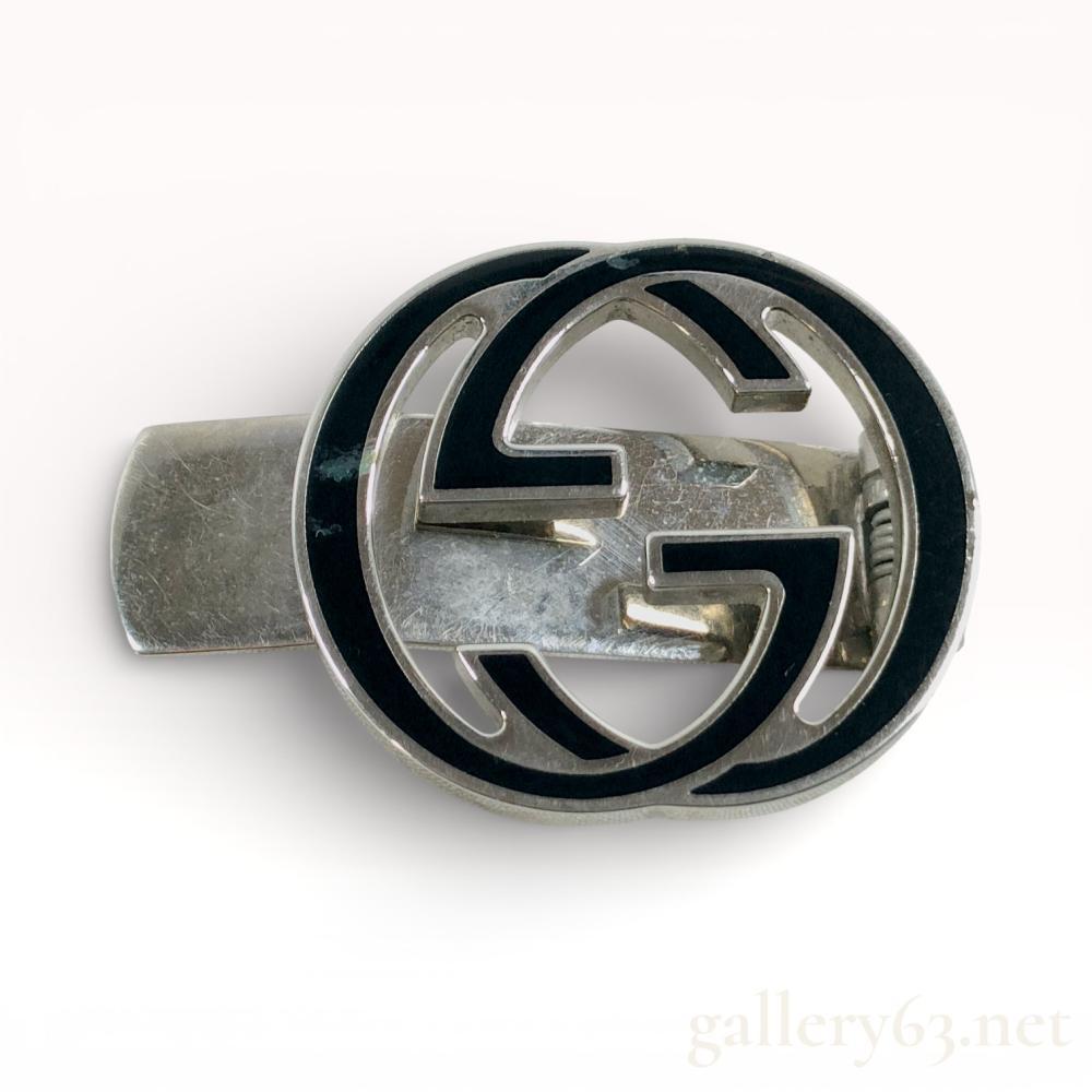 Description
Authentic Gucci Metal money clip featuring the Gucci interlocking G motif with black enamel detailing. Spring clip construction with polished and brushed surfaces. Gucci markings present.