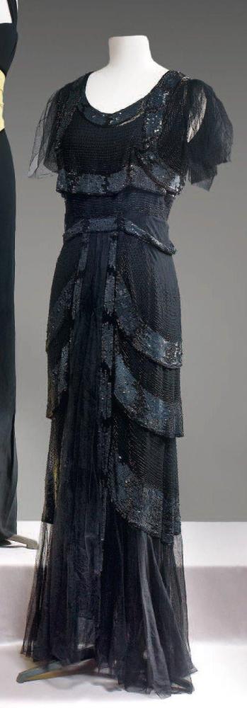 Anonyme

Robe du soir longue en tulle noir partiellement rebrodé de perles tubulaires noires rehaussé de biais recouverts de paillettes noires, encolure ronde, volants de tulle retombant sur l’épaule, jupe fluide à quilles à finition de volants. (fermeture éclair rapportée, petits manques)
