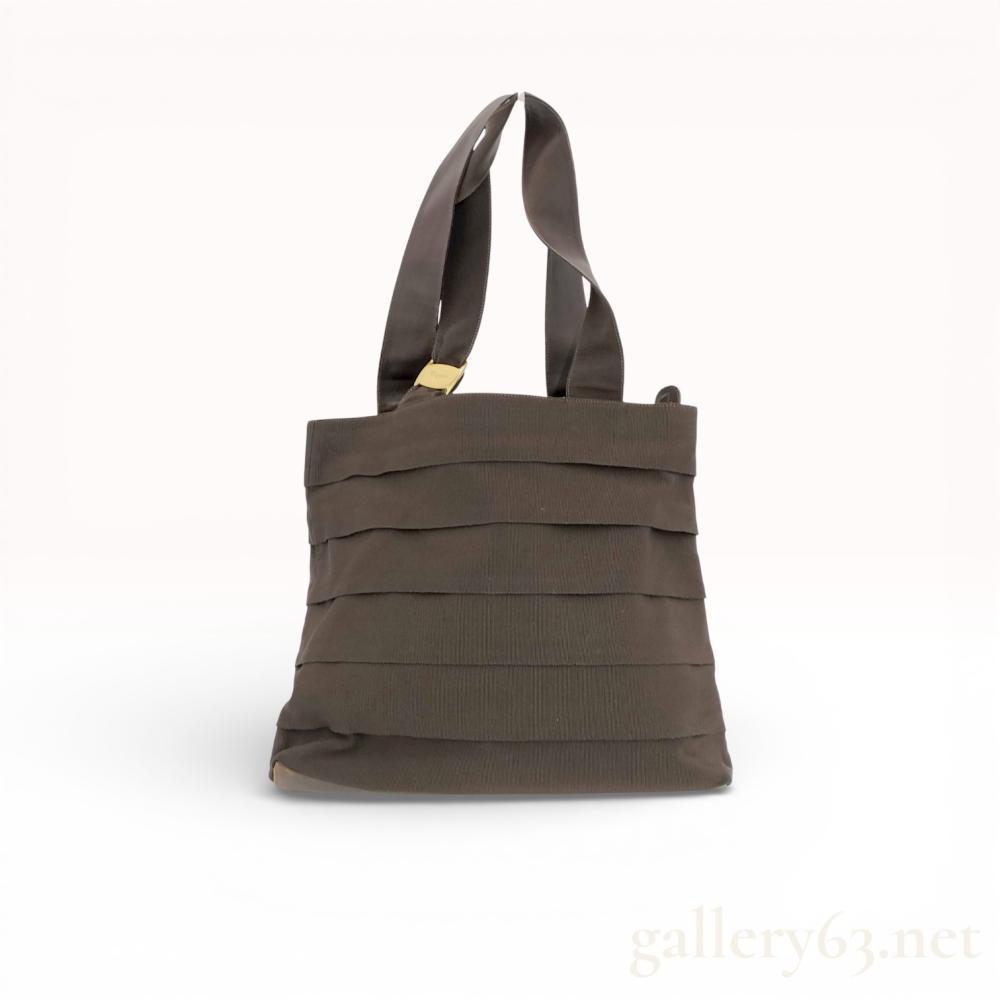 Description
Salvatore Ferragamo tote bag having a rectangular form with open top and double handles. Featuring brown grosgrain fabric exterior with layered horizontal ribbon design. Set with a small gold-tone Vara bow accent at one handle base. Having tonal stitching and soft structure. Interior lined in dark fabric with zip closure and internal pocket.