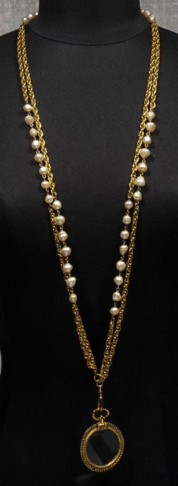 CHANEL

Sautoir composé d’une double chaîne torsadée en métal doré ornée de perles blanches retenant une loupe. Signée