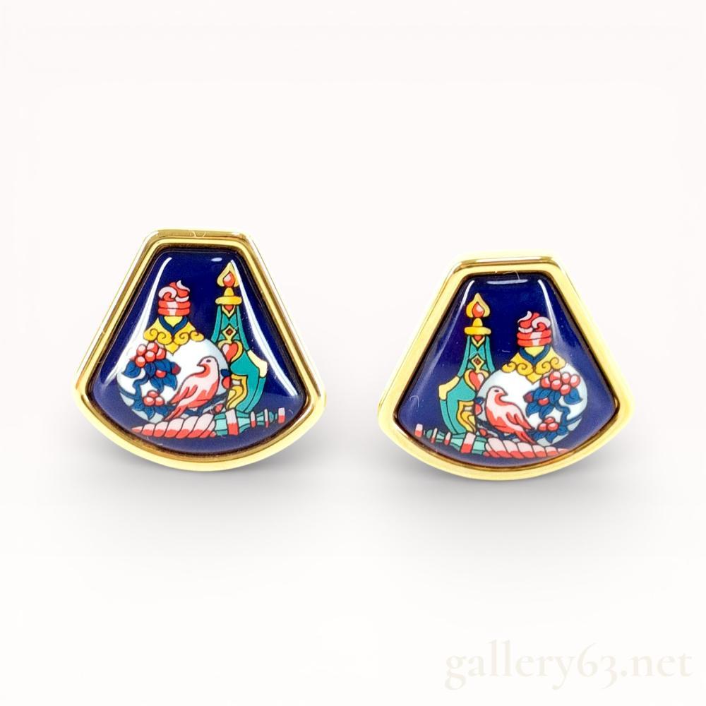 Description
A matched pair of Hermes cloisonne enamel clip-on earrings, late 20th century. Each fan-shaped earring features a mirrored scene of a bird among ceramic vessels and floral motifs on a cobalt blue ground, set within a gold-toned metal frame. The reverse of each earring is stamped HERMES alongside a square hallmark and features hinged lever-back clips with comfort pads. This lot includes the original Hermes Paris presentation box and a soft orange protective pouch.
Width: Approximately 22 mm.