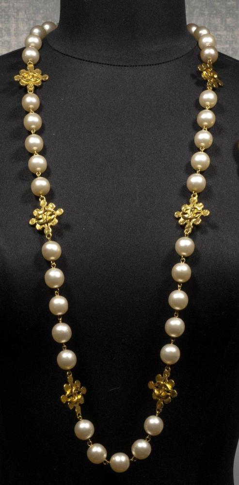 CHANEL

Sautoir composé de perles blanches montées sur motifs en métal doré, siglé. Signé